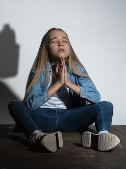 Girl prays for help while sitting against a wall